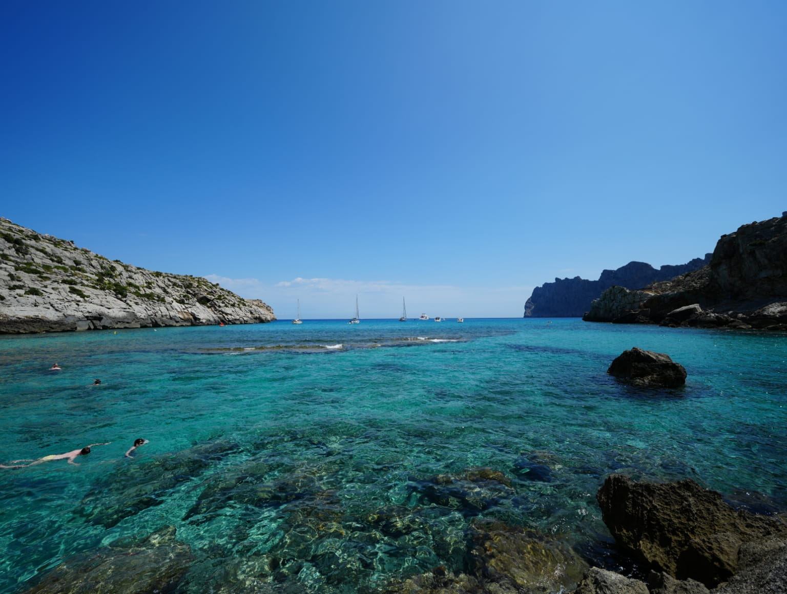 People swimming in the tuquoise blue waters of Cala San Vicente.