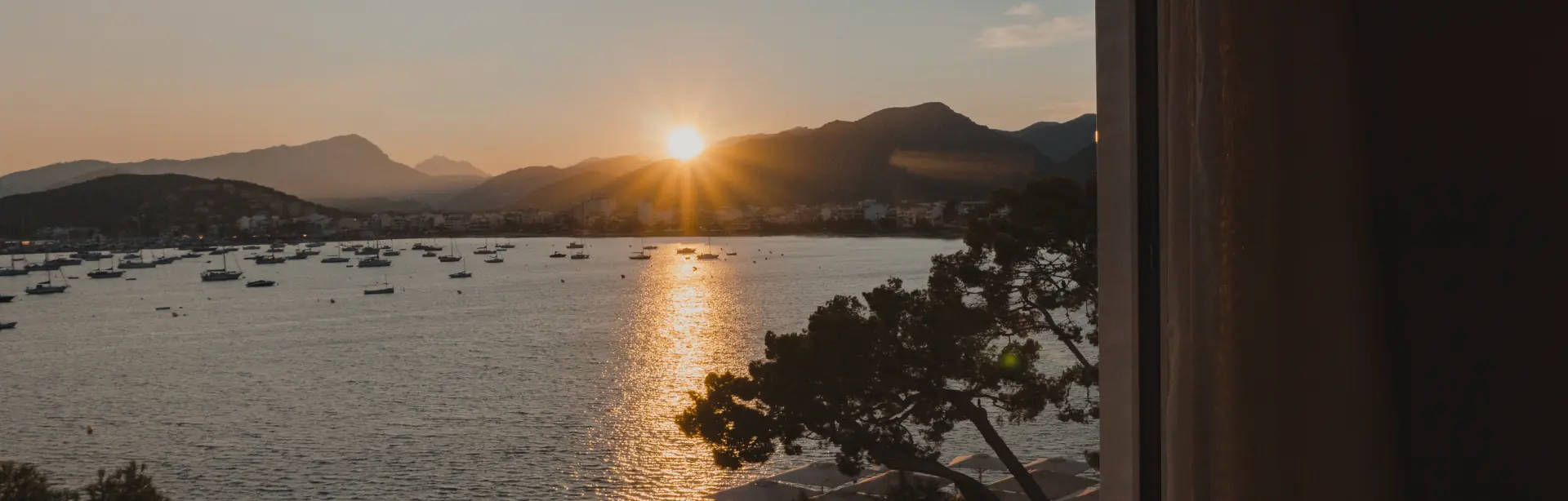 Atardecer sobre una bahía de Mallorca con barcos fondeados y montañas al fondo.